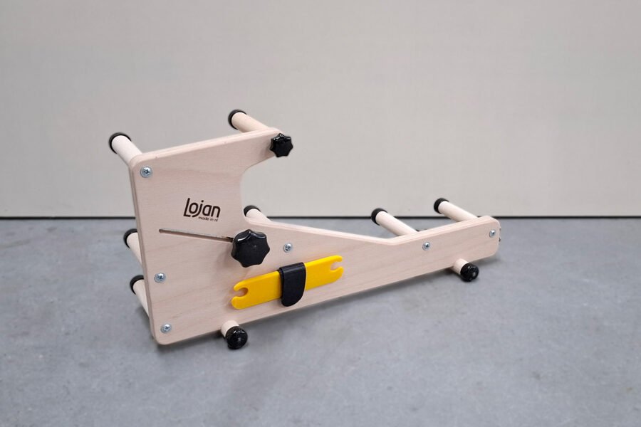 Πλάγια όψη (προφίλ) του μίνι αργαλειού Lojan Inkeltje. Το λογότυπο Lojan είναι καθαρά ορατό στο ξύλινο πάνελ, και η κίτρινη σαΐτα είναι αποθηκευμένη στην ειδική υποδοχή στο πλάι.