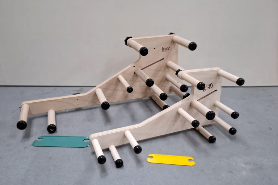 Φωτογραφία προϊόντος που συγκρίνει το μέγεθος του κανονικού αργαλειού Lojan Inkle (πάνω αριστερά) με τον πολύ μικρότερο μίνι αργαλειό Inkeltje (κάτω δεξιά). Μια πράσινη-τιρκουάζ σαΐτα και μια κίτρινη σαΐτα βρίσκονται μπροστά τους.