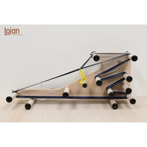 Lojan Inkle 3-1 Πλάγια όψη (προφίλ) του φορητού αργαλειού Inkle 3-1 της Lojan, στημένου πάνω σε ξύλινη επιφάνεια. Ο αργαλειός είναι στημένος με κίτρινα νήματα μιταριών και σκούρο μπλε νήμα, αναδεικνύοντας τη συγκεκριμένη διάταξη των πίρων και την πορεία του νήματος για την κλασική ύφανση inkle.