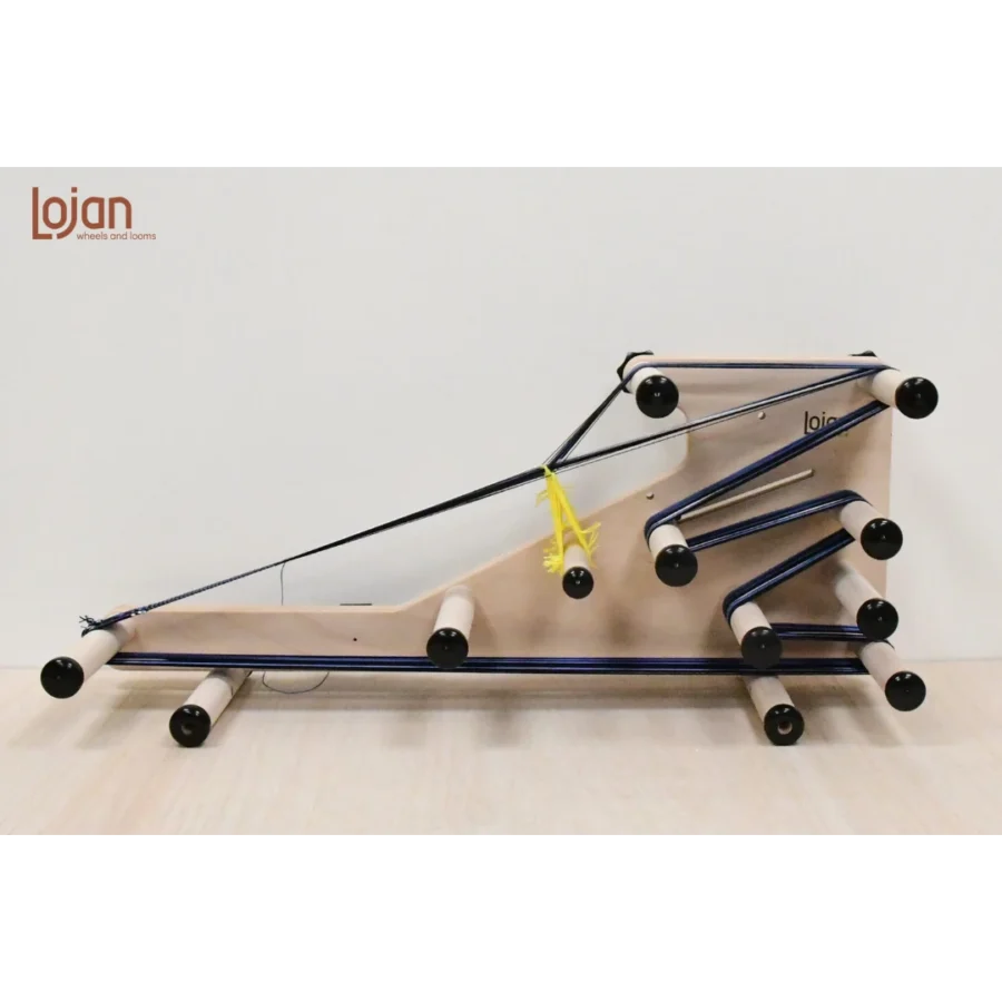 Πλάγια όψη (προφίλ) του φορητού αργαλειού Inkle 3-1 της Lojan, στημένου πάνω σε ξύλινη επιφάνεια. Ο αργαλειός είναι στημένος με κίτρινα νήματα μιταριών και σκούρο μπλε νήμα, αναδεικνύοντας τη συγκεκριμένη διάταξη των πίρων και την πορεία του νήματος για την κλασική ύφανση inkle.