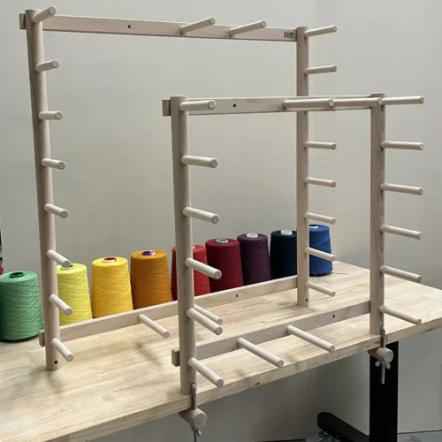 Δύο άδειες ξύλινες διάστρες της Lojan σε διαφορετικά μεγέθη, τοποθετημένες πάνω σε ένα ξύλινο τραπέζι εργασίας. Η μικρότερη διάστρα είναι στερεωμένη στην μπροστινή άκρη, ενώ η μεγαλύτερη βρίσκεται από πίσω. Ανάμεσά τους υπάρχει μια σειρά από πολύχρωμους κώνους νήματος.