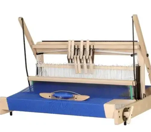 Louet Jane επιτραπέζιος αργαλειός Μια φωτογραφία σε λευκό φόντο του επιτραπέζιου αργαλειού Louët Jane με 8 μιτάρια. Ο αργαλειός είναι στημένος με έντονο μπλε νήμα, και μια ξύλινη σαΐτα βάρκα με μπλε μασούρι ακουμπά πάνω στο υφασμένο τμήμα. Ο μηχανισμός με τους μοχλούς χειρισμού των μιταριών και τα μιτάρια διακρίνονται καθαρά.