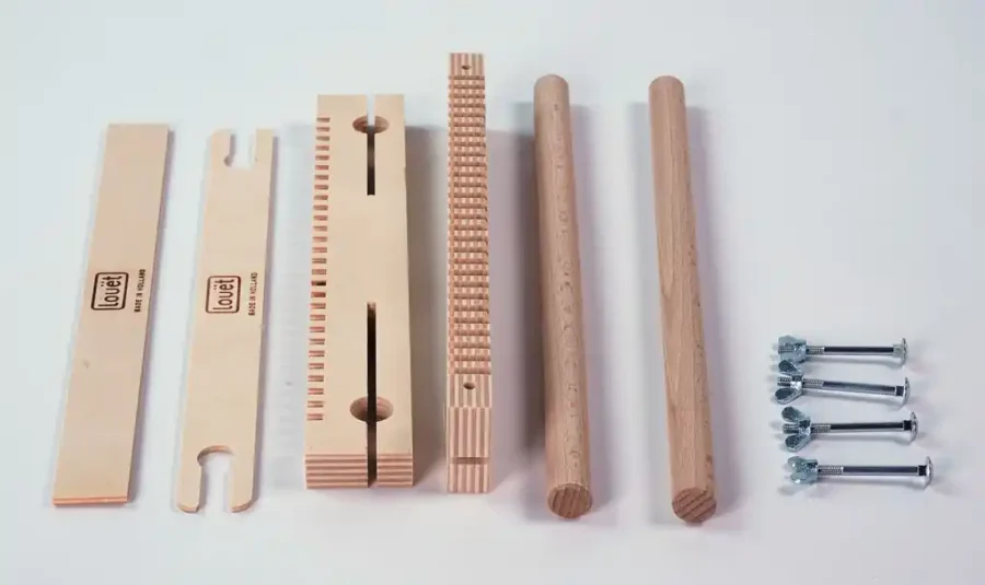 Louet Lisa τα μέρη του μικρού αργαλειού Μια φωτογραφία με όλα τα εξαρτήματα του μικρού τελάρου υφαντικής Louët Lisa πριν τη συναρμολόγηση, τακτοποιημένα σε λευκό φόντο. Περιλαμβάνει τα ξύλινα μέρη με το λογότυπο της Louët (οδοντωτές μπάρες στημονιού, στρογγυλούς πλευρικούς πείρους, μια επίπεδη σαΐτα και ένα ξύλινο εργαλείο) καθώς και τέσσερις μεταλλικές βίδες με πεταλούδες για την ένωση.