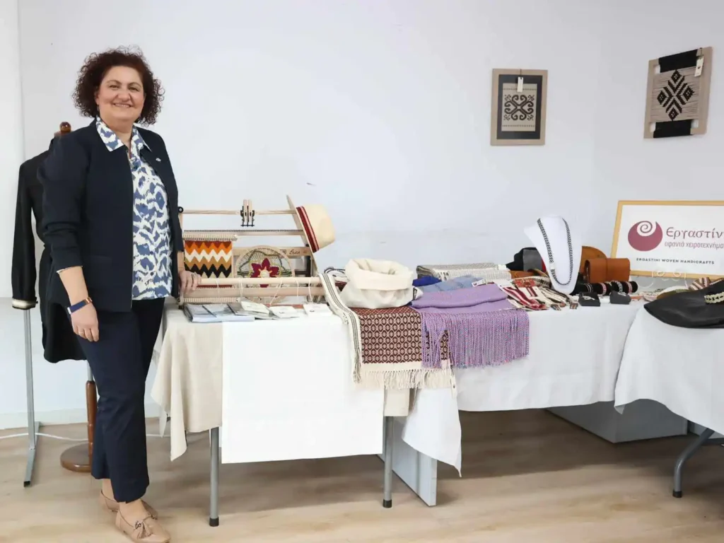Η Ζωή μπροστά από τον πάγκο με τα υφαντά χειροτεχνήματα της Εργαστίνης