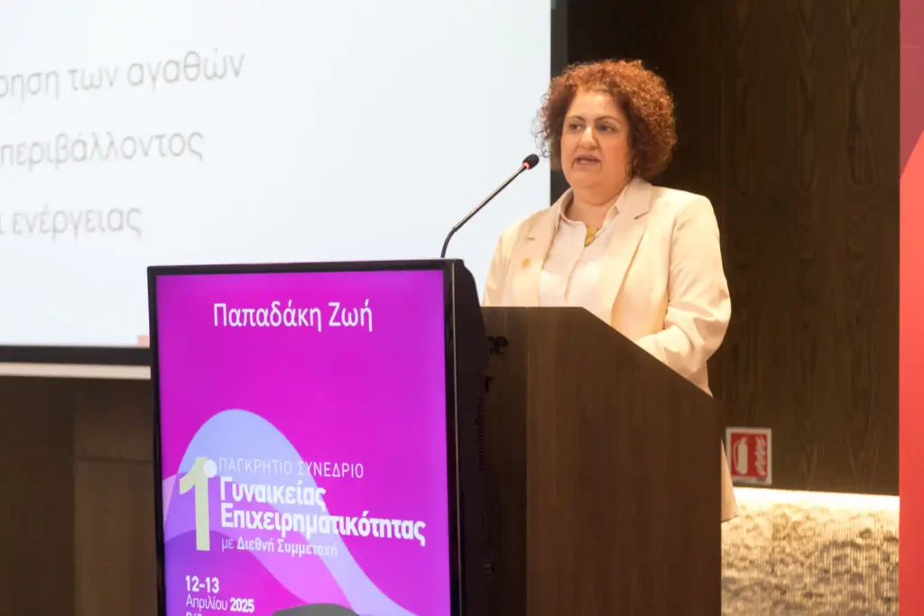 Η Ζωή Παπαδάκη στο βήμα του 1ου Παγκρήτιου Συνεδρίου Γυναικείας Επιχειρηματικότητας, παρουσιάζοντας το θέμα «Υφαίνοντας το μέλλον». Στο ψηφιακό βήμα προβάλλεται το λογότυπο του συνεδρίου, ενώ στο βάθος φαίνεται μέρος των διαφανειών της παρουσίασής της στην οθόνη προβολής.